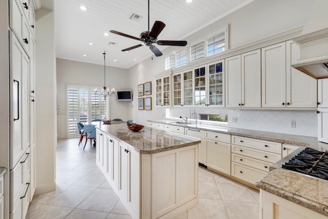 kitchen featuring a kitchen island, tasteful backsplash, ceiling fan with notable chandelier, and light stone counters