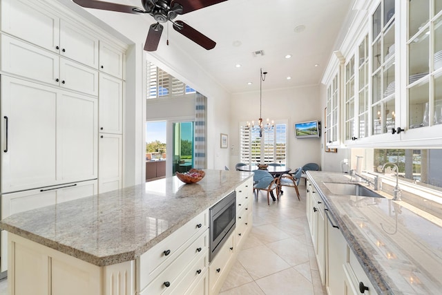 kitchen featuring pendant lighting, stainless steel microwave, sink, a center island, and light stone countertops