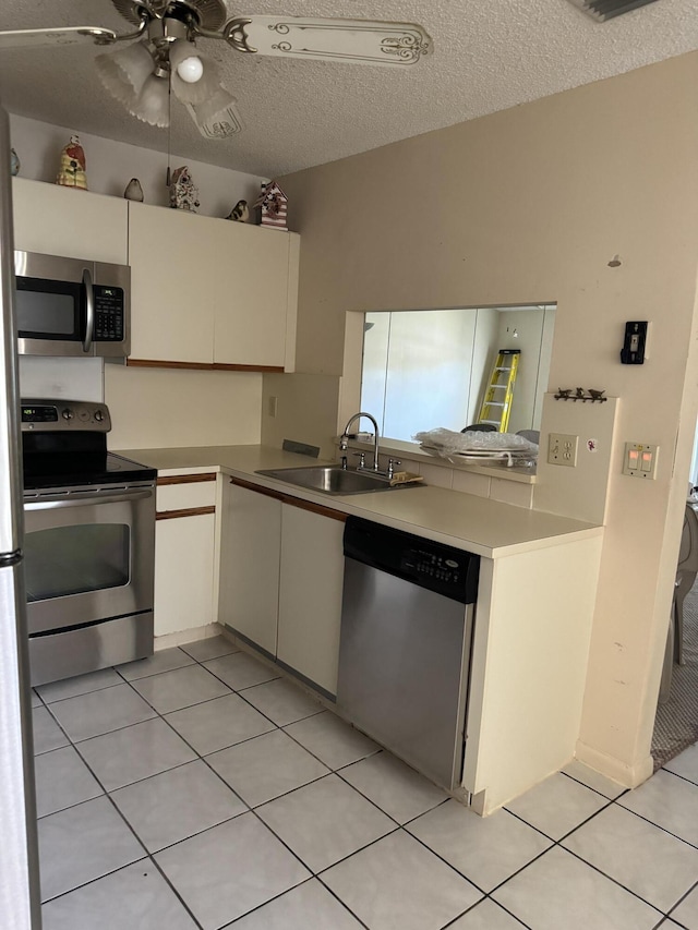 kitchen featuring appliances with stainless steel finishes, a textured ceiling, ceiling fan, sink, and light tile patterned floors