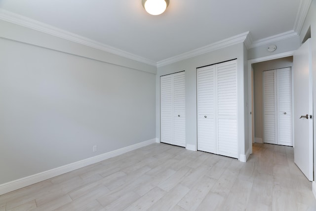 unfurnished bedroom featuring crown molding, light wood-type flooring, and multiple closets