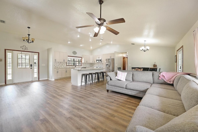 living room with lofted ceiling, ceiling fan with notable chandelier, and light wood-type flooring