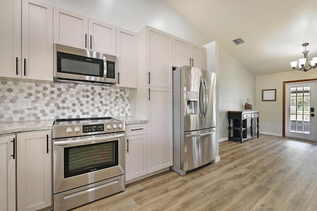 kitchen featuring stainless steel appliances, vaulted ceiling, white cabinetry, and light stone counters