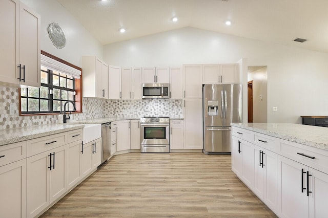 kitchen with high vaulted ceiling, white cabinetry, sink, light stone counters, and stainless steel appliances