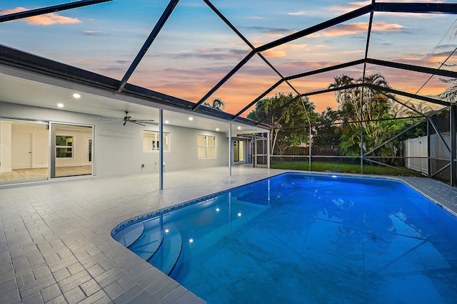 pool at dusk with a lanai, a patio area, and ceiling fan