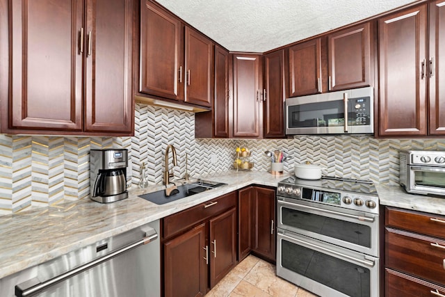 kitchen featuring stainless steel appliances, a textured ceiling, sink, backsplash, and light stone counters