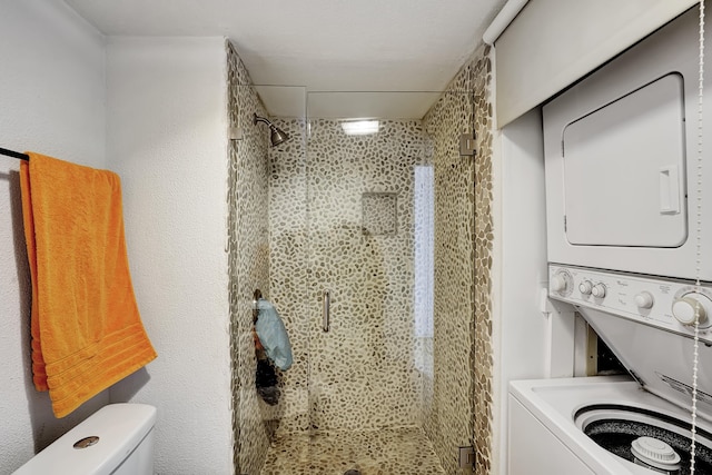 bathroom featuring an enclosed shower, stacked washer and clothes dryer, and toilet