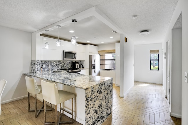 kitchen featuring white cabinetry, decorative light fixtures, stainless steel appliances, light parquet floors, and a breakfast bar area