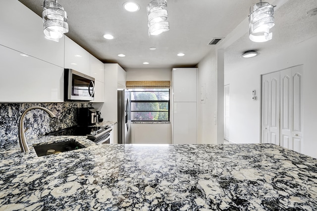 kitchen featuring pendant lighting, white cabinetry, appliances with stainless steel finishes, and dark stone counters