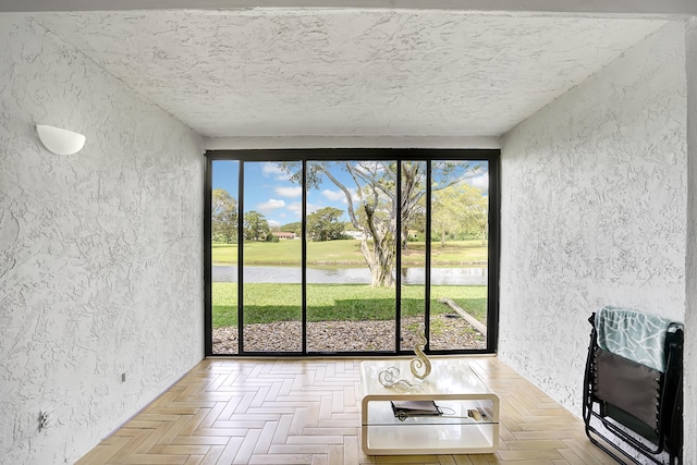 unfurnished living room featuring a water view, a textured ceiling, and light parquet floors