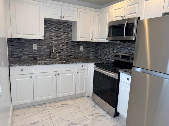 kitchen featuring dark stone counters, marble finish floor, stainless steel appliances, white cabinetry, and a sink