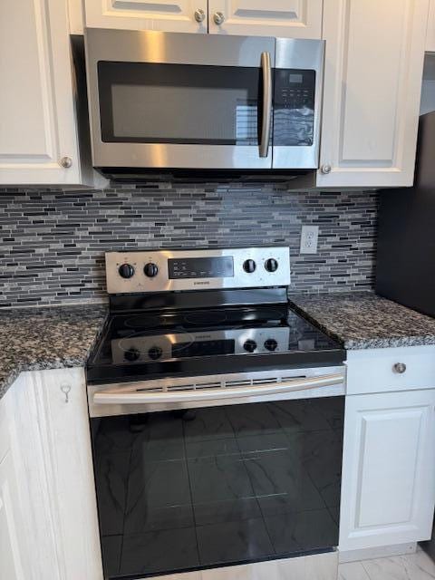 kitchen with appliances with stainless steel finishes, dark stone counters, white cabinetry, and backsplash