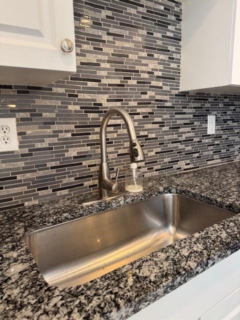 interior details featuring dark stone counters, a sink, white cabinets, and decorative backsplash