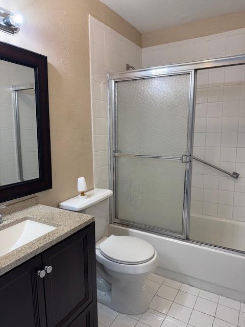 full bathroom with bath / shower combo with glass door, a textured wall, toilet, vanity, and tile patterned flooring