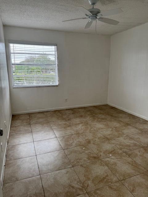 tiled spare room featuring a ceiling fan, a textured ceiling, and baseboards