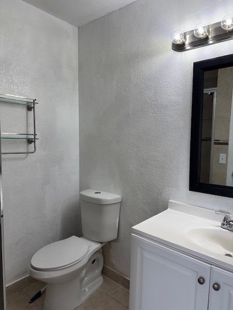 bathroom featuring a textured wall, tile patterned flooring, toilet, vanity, and baseboards