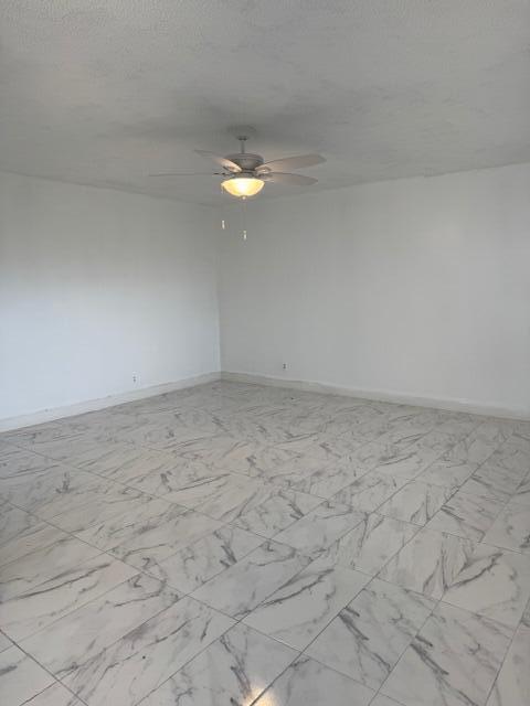 spare room with marble finish floor, a ceiling fan, baseboards, and a textured ceiling