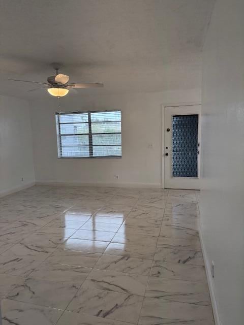 spare room featuring a ceiling fan, marble finish floor, and baseboards