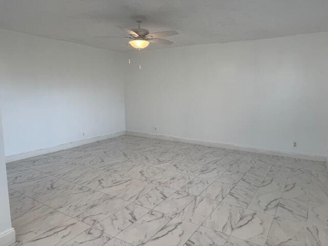 empty room with marble finish floor, a ceiling fan, and baseboards