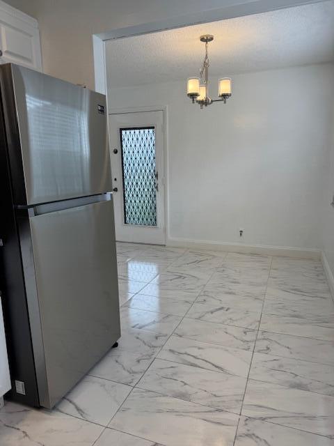 unfurnished dining area with a textured ceiling, marble finish floor, an inviting chandelier, and baseboards