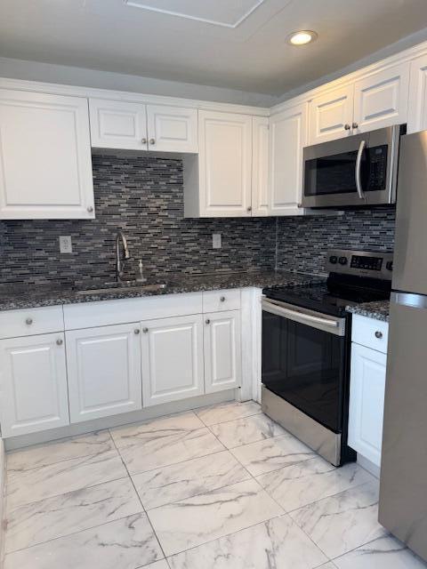 kitchen with marble finish floor, stainless steel appliances, white cabinets, a sink, and dark stone counters