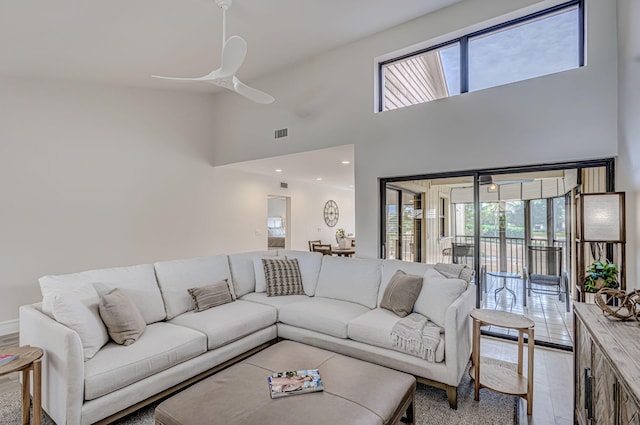 living room with ceiling fan, light hardwood / wood-style flooring, and a towering ceiling