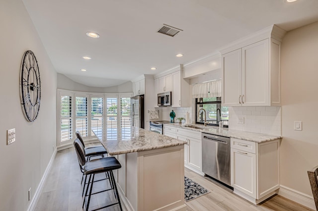 kitchen with sink, stainless steel appliances, tasteful backsplash, white cabinetry, and a center island