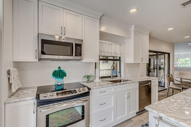 kitchen featuring white cabinetry, backsplash, sink, stainless steel appliances, and light stone counters