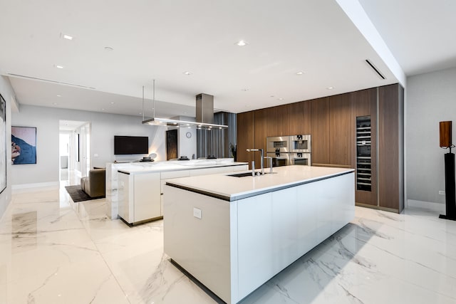 kitchen featuring an island with sink, double oven, light tile flooring, dark brown cabinets, and sink