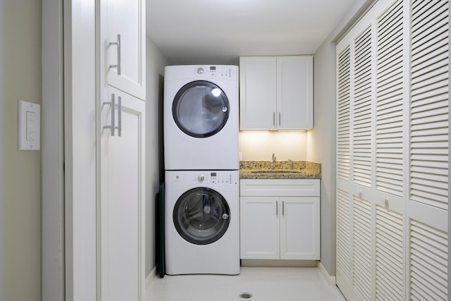 laundry room with stacked washer / dryer, light tile floors, cabinets, and sink