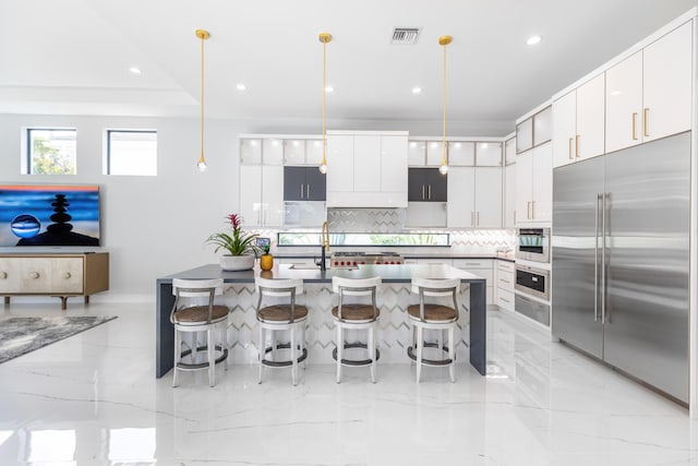 kitchen featuring tasteful backsplash, stainless steel built in refrigerator, pendant lighting, a kitchen bar, and white cabinets