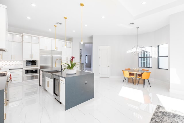 kitchen featuring a kitchen island with sink, white cabinets, hanging light fixtures, wine cooler, and tasteful backsplash