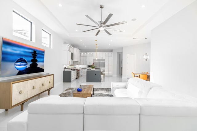 living room with ceiling fan with notable chandelier and a raised ceiling