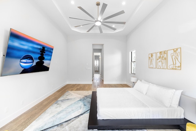 bedroom featuring ceiling fan, light wood-type flooring, and a tray ceiling