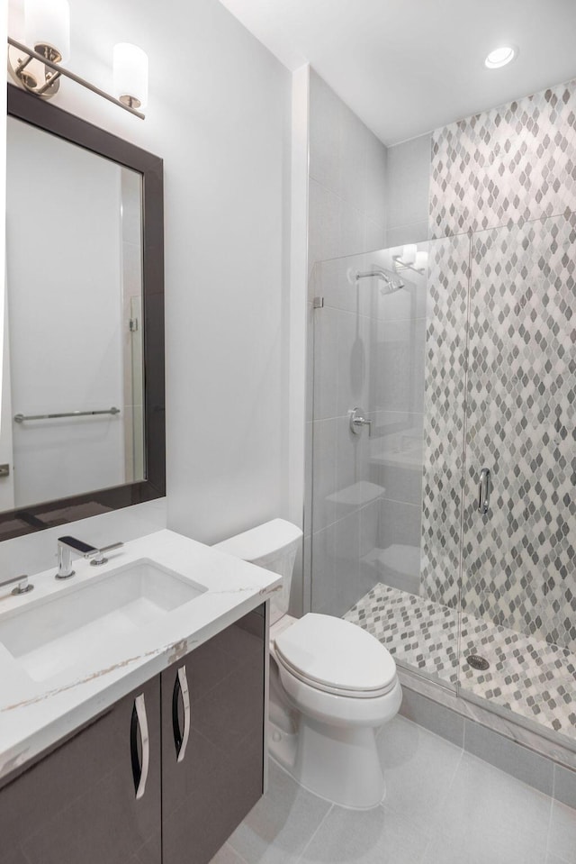 bathroom featuring toilet, vanity, tile patterned floors, and a shower with door