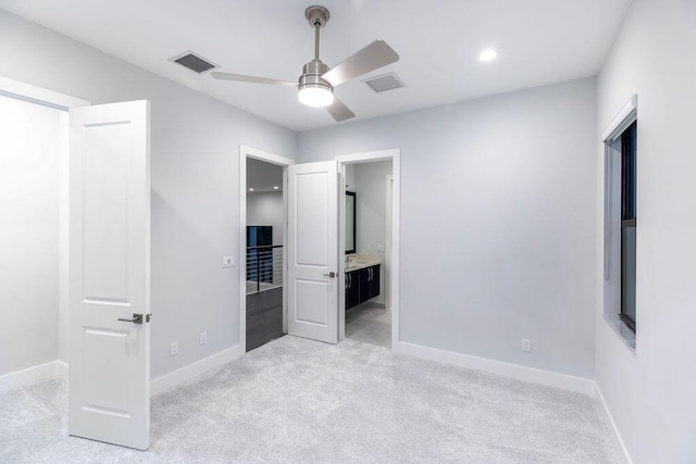 unfurnished bedroom featuring ensuite bath, ceiling fan, light colored carpet, and a spacious closet