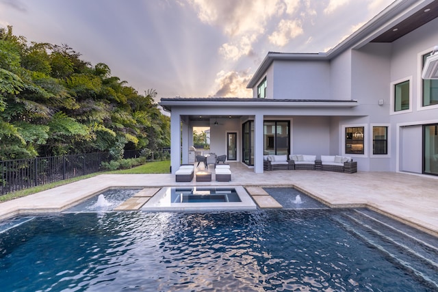 pool at dusk featuring ceiling fan, an outdoor hangout area, pool water feature, an in ground hot tub, and a patio