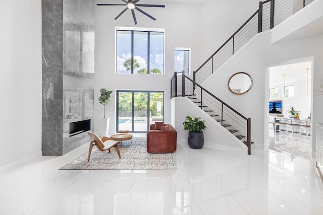 living room with ceiling fan, a high ceiling, and a tiled fireplace