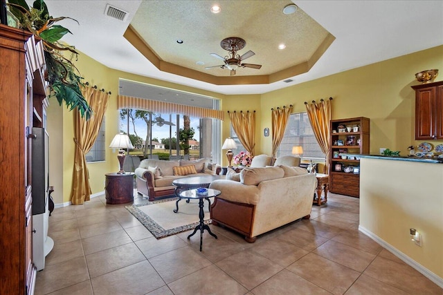 tiled living room with a tray ceiling and ceiling fan