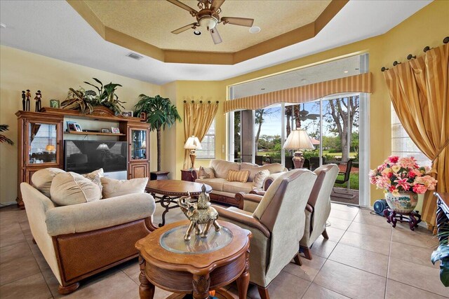 living room with light tile floors, a raised ceiling, and ceiling fan