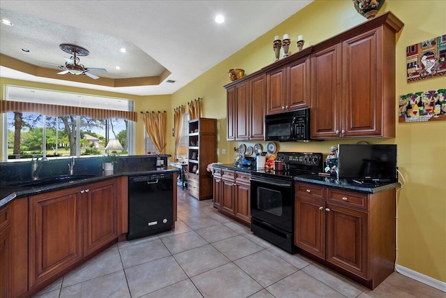 kitchen featuring sink, ceiling fan, dark stone countertops, a tray ceiling, and black appliances