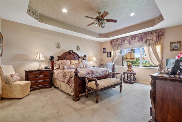 carpeted bedroom featuring a textured ceiling, ceiling fan, and a tray ceiling