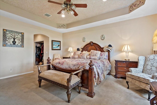 carpeted bedroom featuring ceiling fan, a raised ceiling, a walk in closet, a textured ceiling, and a closet