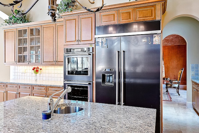 kitchen featuring light stone countertops, backsplash, sink, and stainless steel appliances