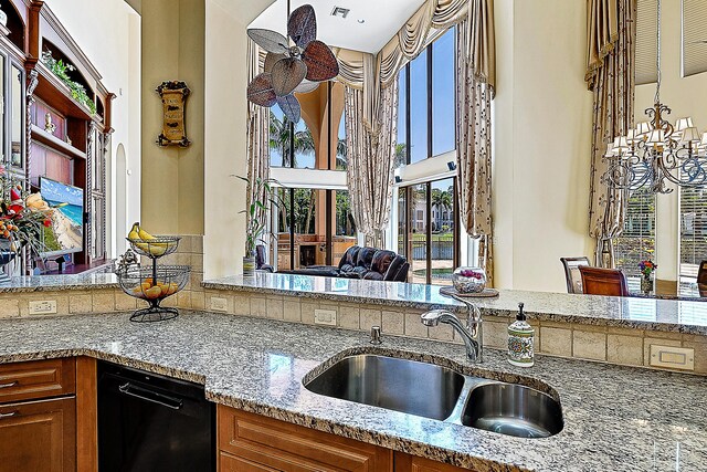 kitchen with ceiling fan, black appliances, sink, an island with sink, and light stone counters