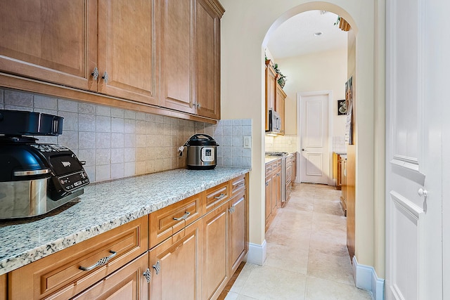 kitchen featuring light tile patterned floors, appliances with stainless steel finishes, light stone counters, and tasteful backsplash