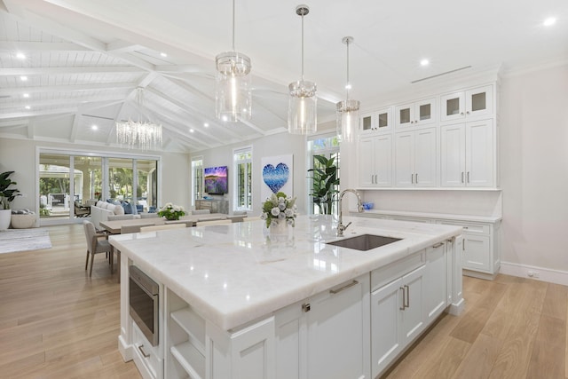 kitchen featuring lofted ceiling with beams, light wood-type flooring, a kitchen island with sink, white cabinetry, and stainless steel microwave