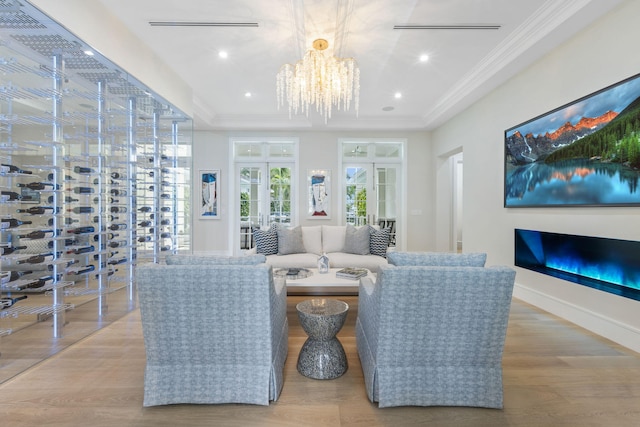 living room featuring a raised ceiling, french doors, light hardwood / wood-style flooring, an inviting chandelier, and crown molding