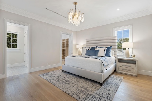 bedroom featuring an inviting chandelier, crown molding, light hardwood / wood-style floors, and a spacious closet