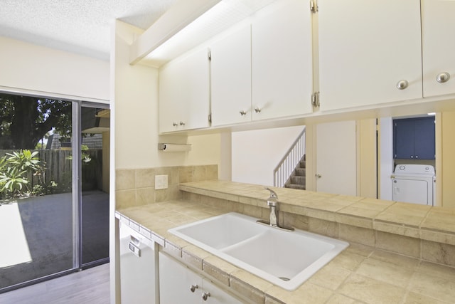 kitchen featuring sink, washer / clothes dryer, a textured ceiling, tile countertops, and white cabinetry