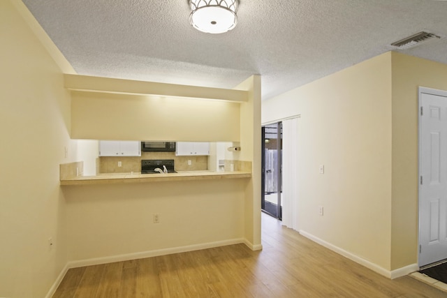 kitchen with range, white cabinetry, light wood-type flooring, and a textured ceiling